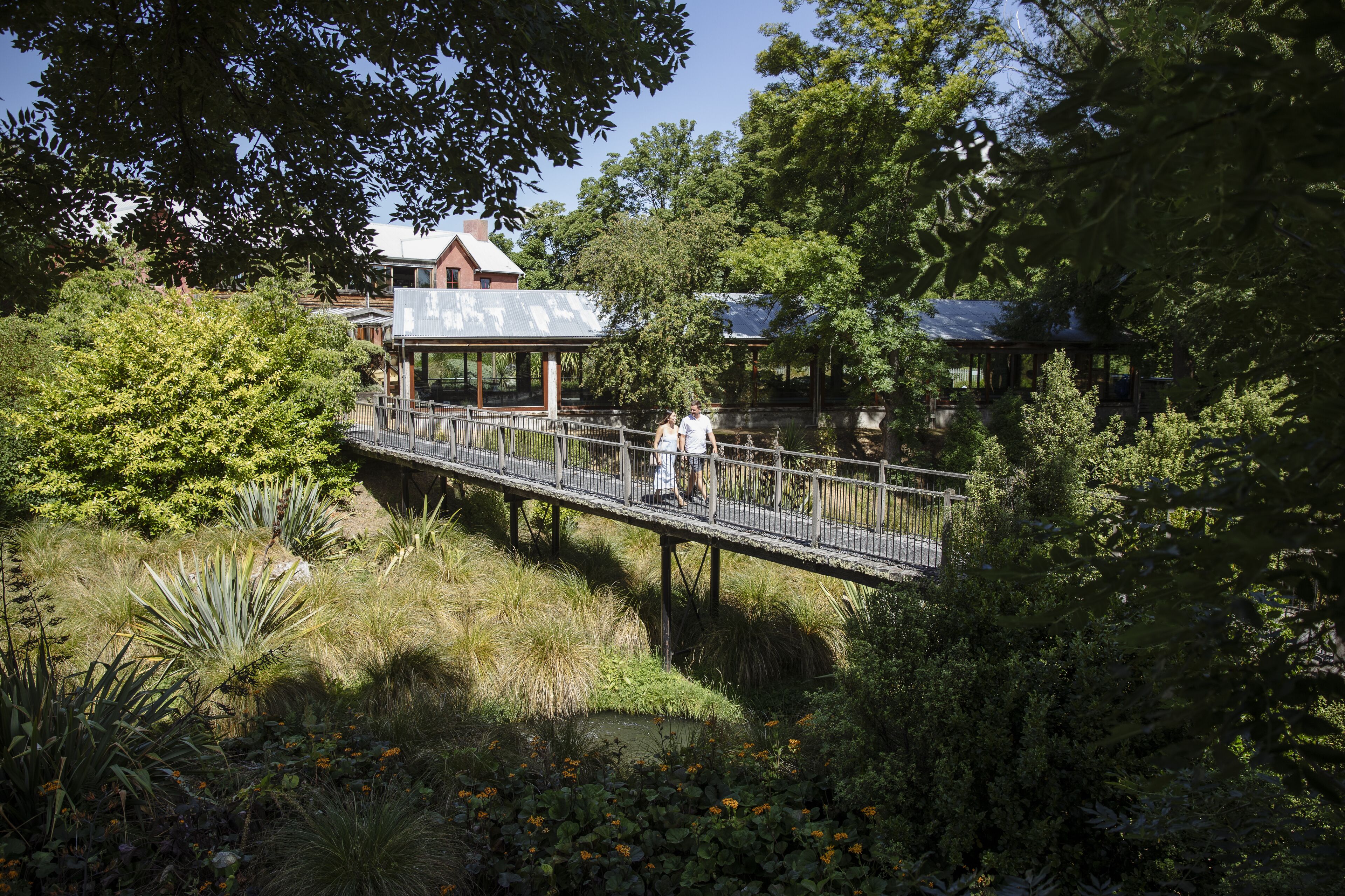 A wooden bridge over a pond with a gazebo and a building in the background.