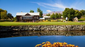 A rustic lodge with a stone wall and a pond in front. - Millbrook Resort (Arrowtown)