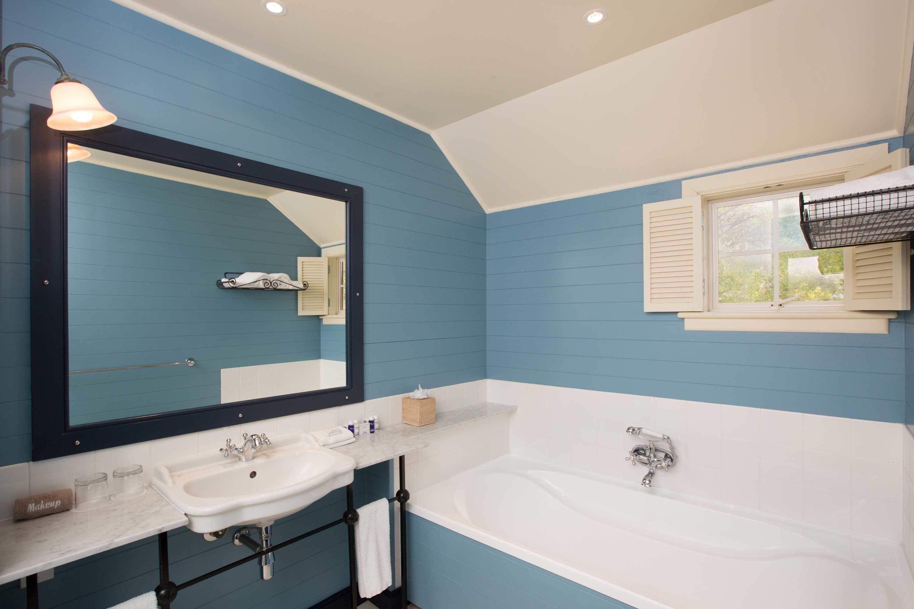 A bathroom with a large mirror, two sinks, a bathtub, and a window with shutters.