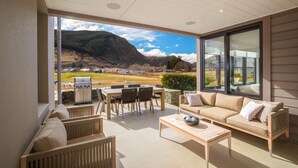A spacious balcony with a dining area, a sofa, and a grill, overlooking a mountainous landscape. - Millbrook Resort (Arrowtown)