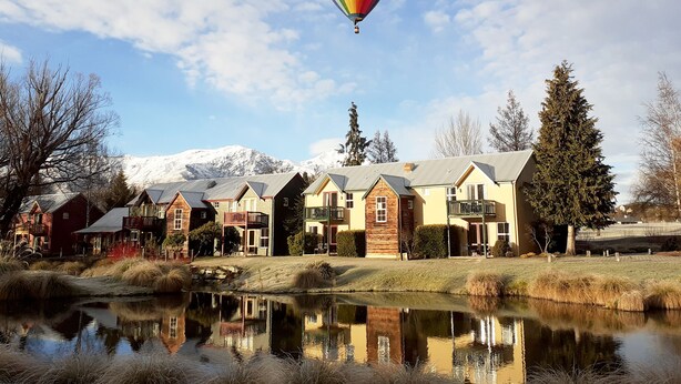 A row of cabins with a mountain backdrop and a hot air balloon in the sky. - Millbrook Resort (Arrowtown)