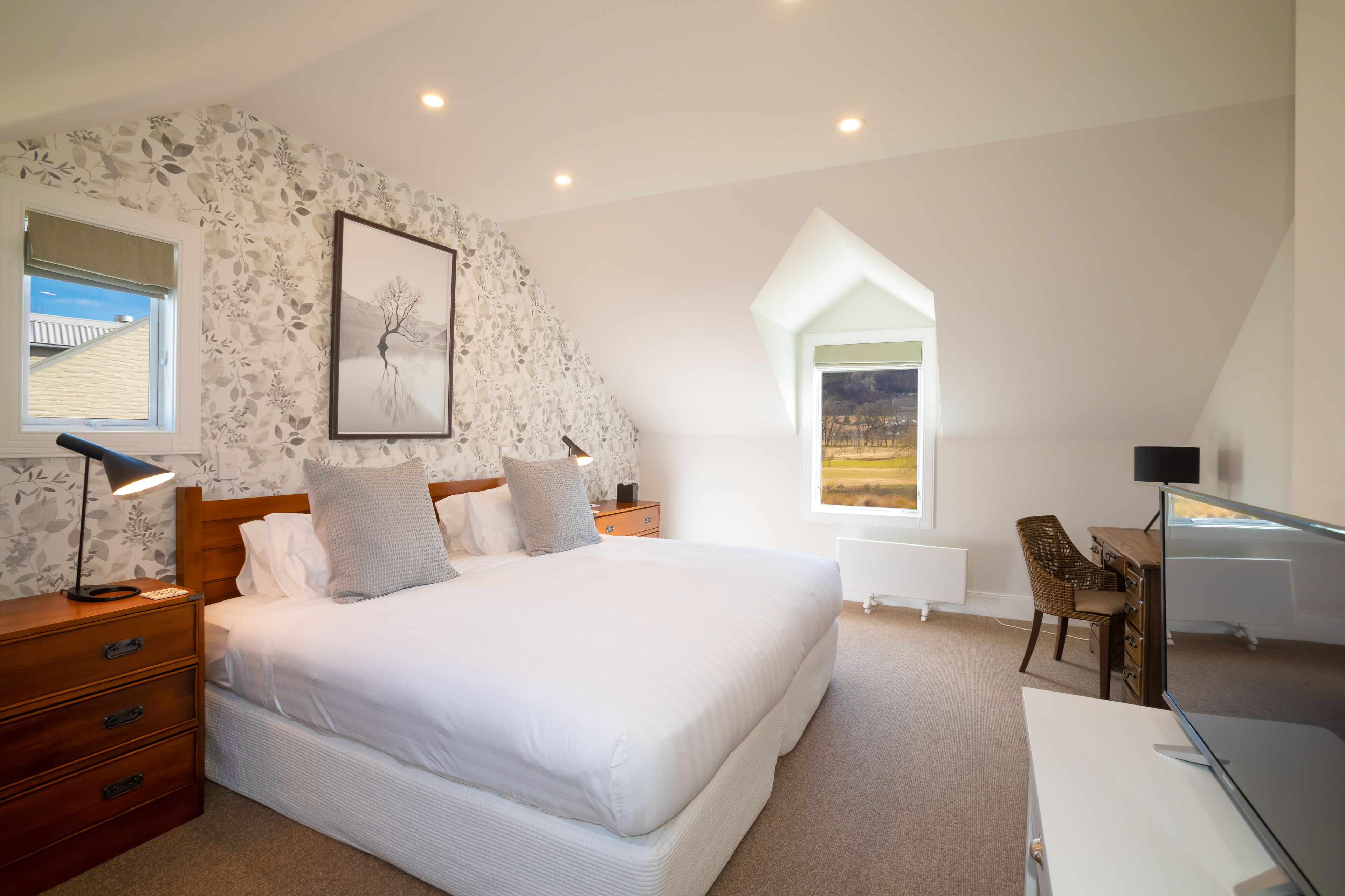 A bedroom with a large bed, a desk, a chair, a window with a view, and a radiator.
