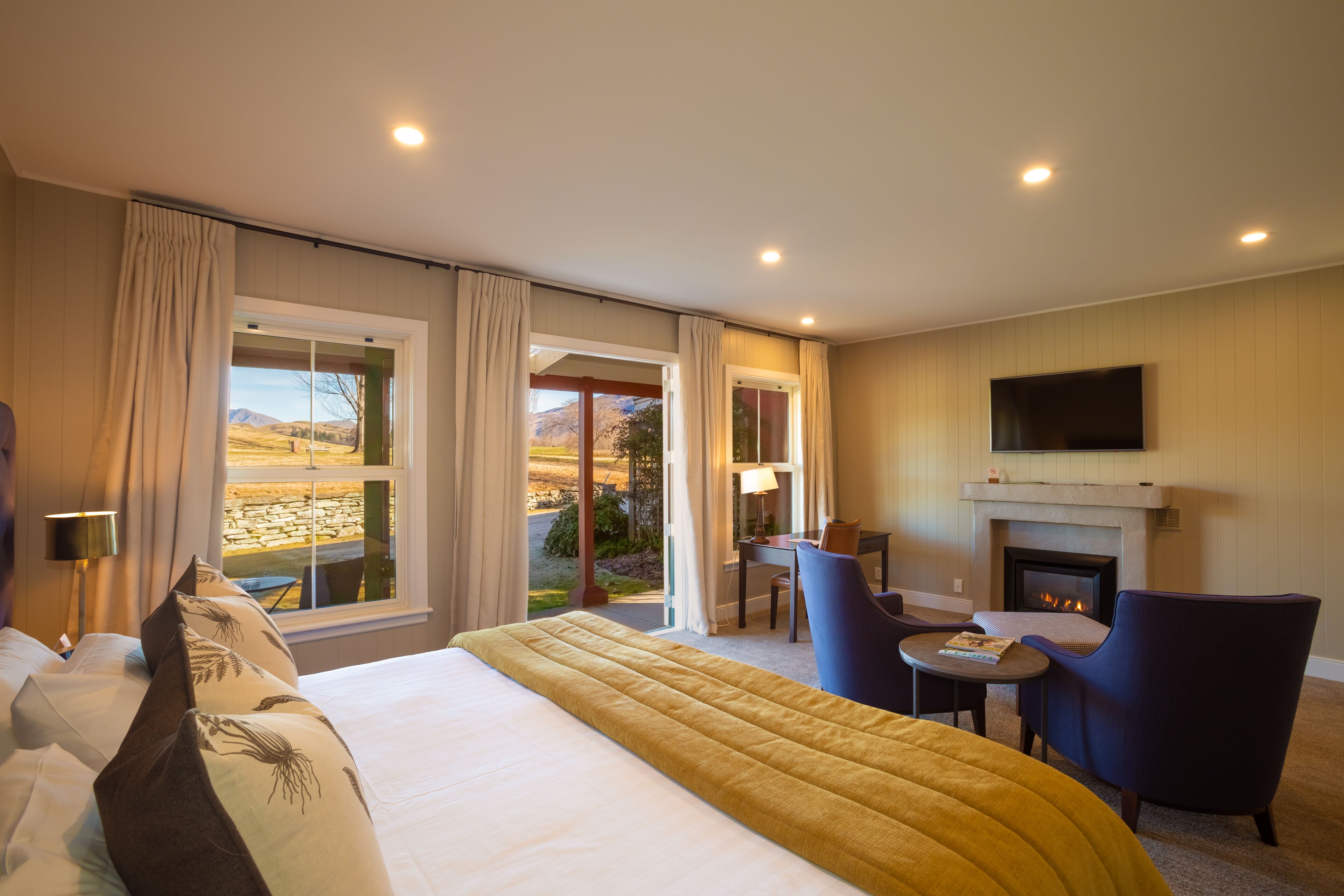 A hotel room with a large bed, a fireplace, a TV, and a view of the outdoors.