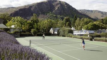 Ein Tennisplatz mit Bergelandschaft im Hintergrund, umgeben von Bäumen und einer Steinmauer.