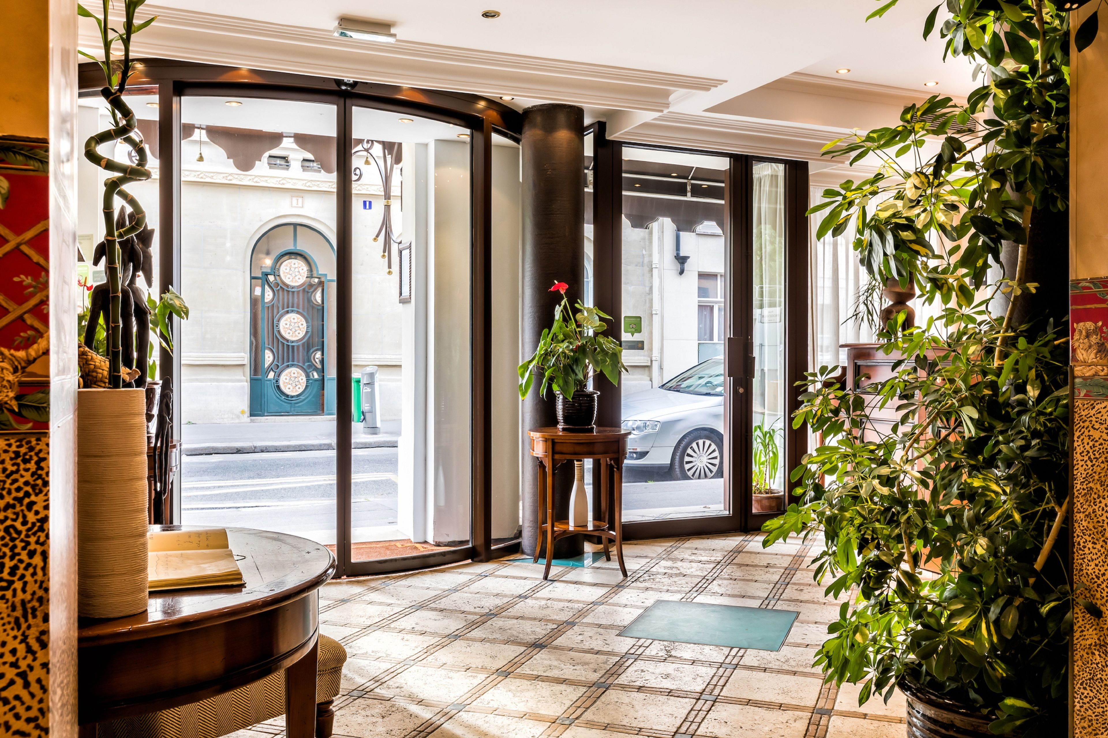 Et hotel lobby med et ternet gulv, et træbord, en potteplante og udsigt til gaden gennem store glasdøre.