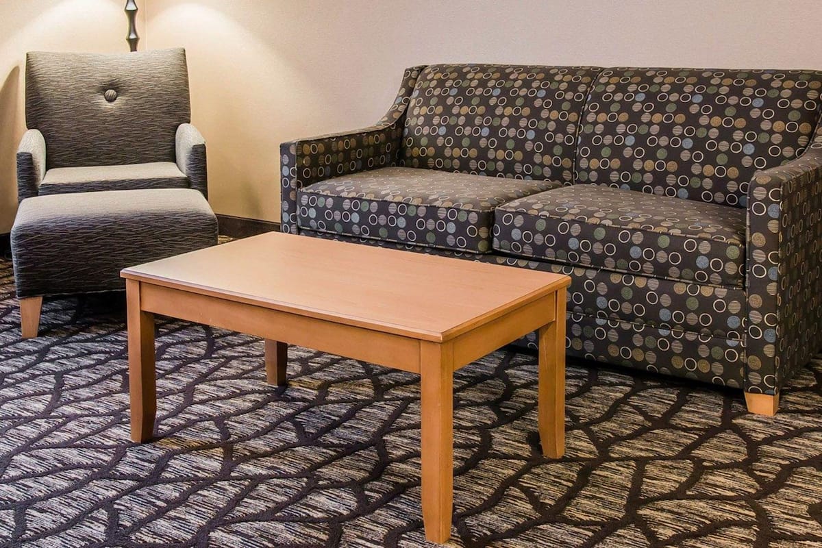 A hotel room with a patterned sofa, a wooden table, and a lamp.