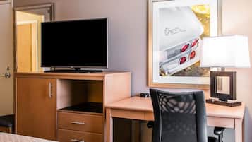 A hotel room with a bed, a desk with a television, a chair, a desk lamp, and a framed picture of a car.