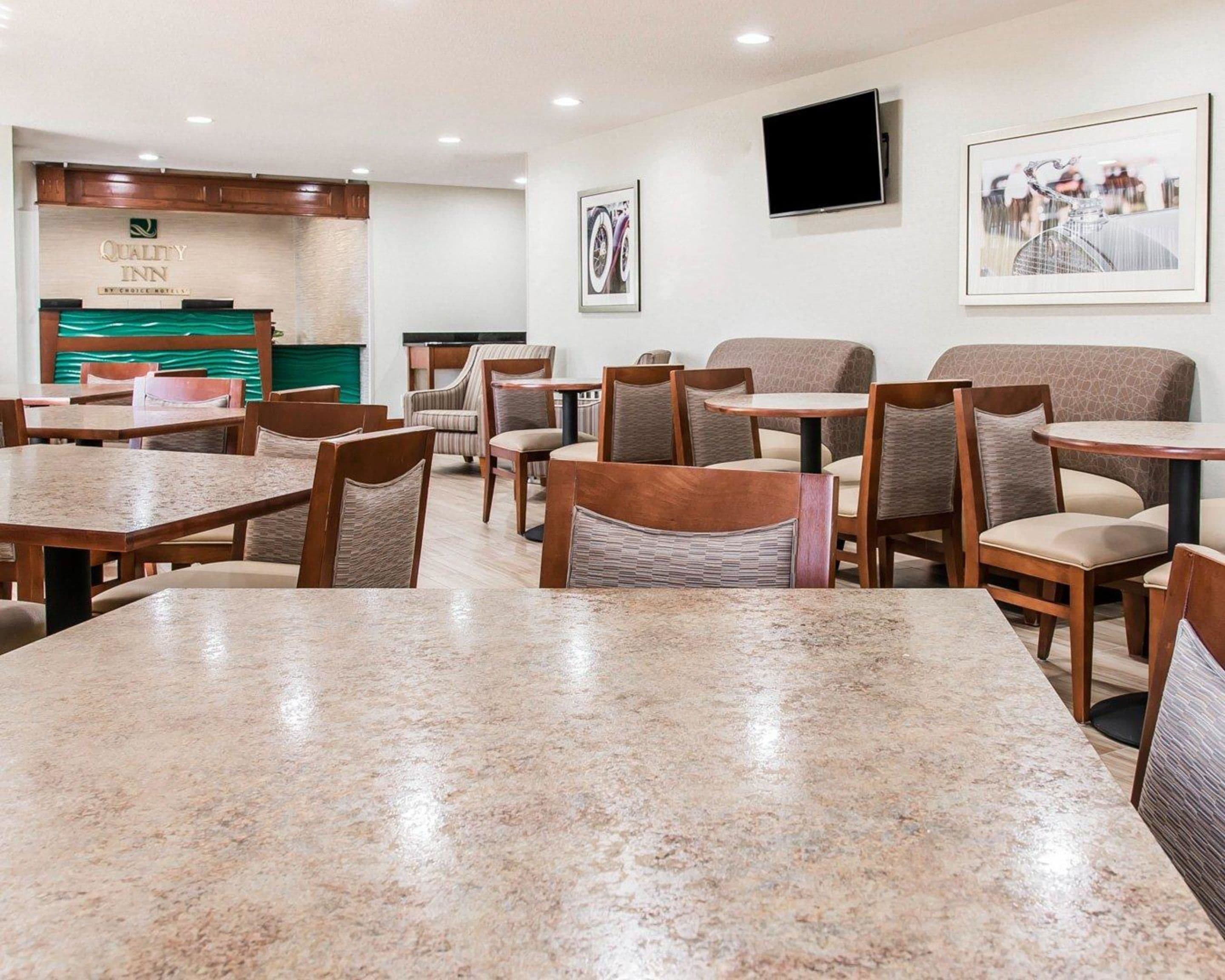 A hotel lobby with wooden tables and chairs, a reception desk, and framed pictures on the walls.