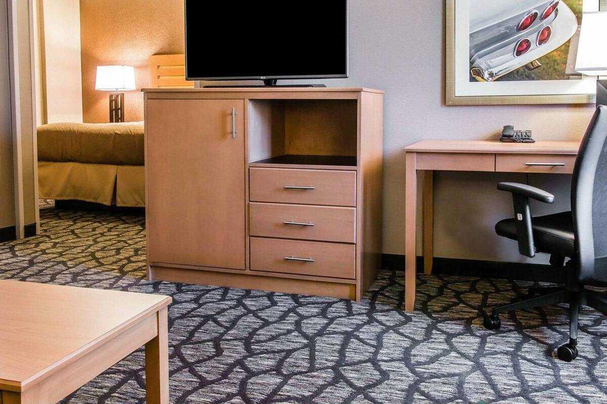 A hotel room with a bed, a desk with a chair, a television, and a framed picture on the wall.