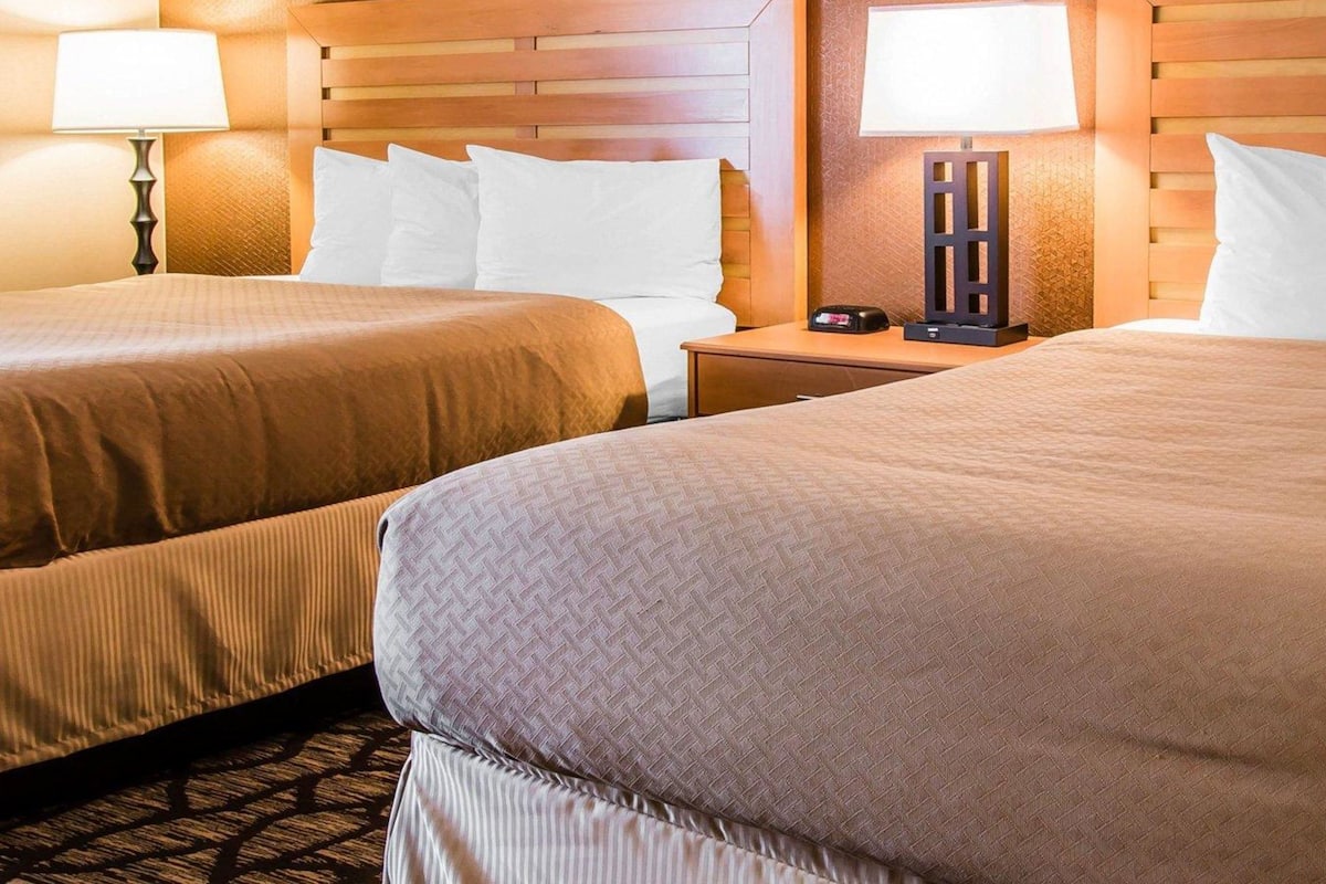A hotel room with two beds, a nightstand, and a lamp.