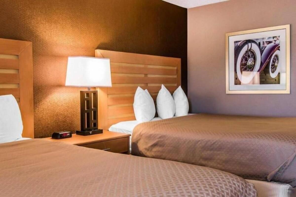 A hotel room with two beds, a nightstand with a lamp, a wall-mounted clock, and a framed picture on the wall.