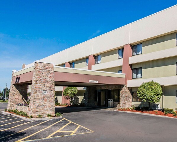A multi-story hotel with a covered entrance, stone pillars, and a parking lot.