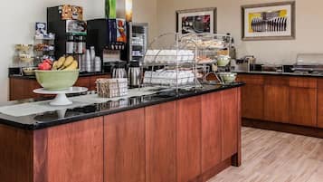 A hotel breakfast area with a wooden counter, coffee machines, a fruit bowl, and a buffet setup.