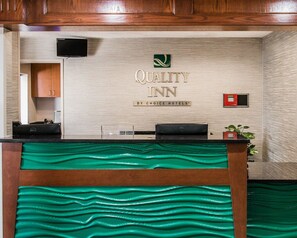 A reception desk with a "Quality Inn" sign, a Dell computer, and a small plant. - Quality Inn & Suites Warren - Detroit (Warren)