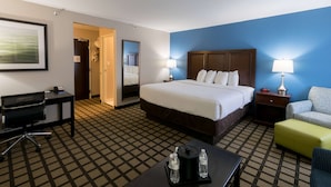 A hotel room with a large bed, a desk, a chair, a nightstand, and a lamp. - Baymont by Wyndham Detroit Airport/Romulus (Romulus)