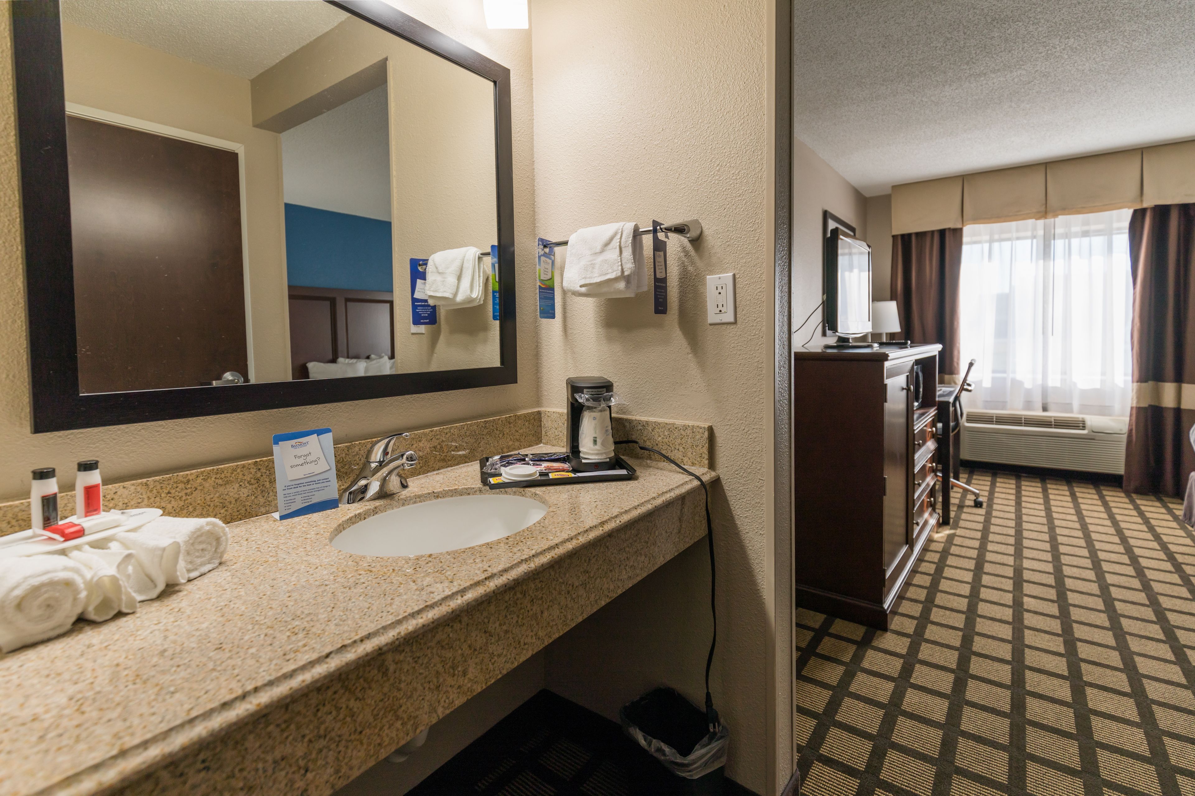 A hotel bathroom with a sink, mirror, towel rack, and a coffee maker.