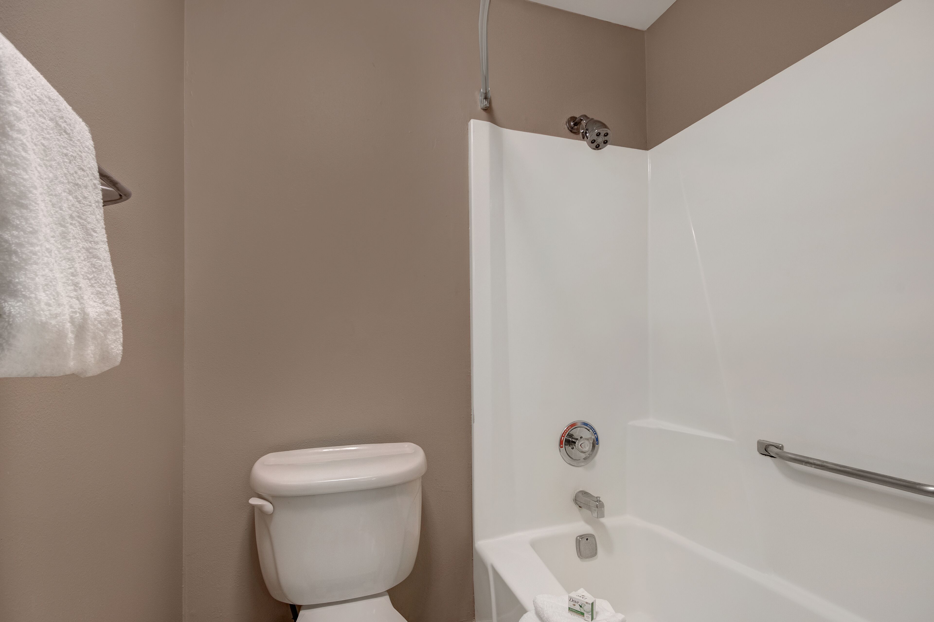 Un bagno con un water, una doccia dotata di maniglia di sostegno e un asciugamano appeso al muro.