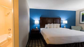 A hotel room with a large bed, two bedside lamps, a wooden headboard, a chair, and a bathroom with a bathtub.