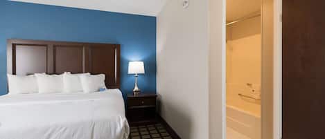 Habitación de hotel con cama, mesita de noche con lámpara, zona de ducha y suelo estampado.