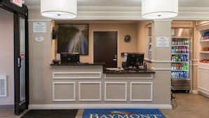 A Baymont Inn & Suites reception area with a check-in counter, a refrigerator stocked with beverages, and a clock on the wall. - Baymont by Wyndham Detroit Airport/Romulus (Romulus)
