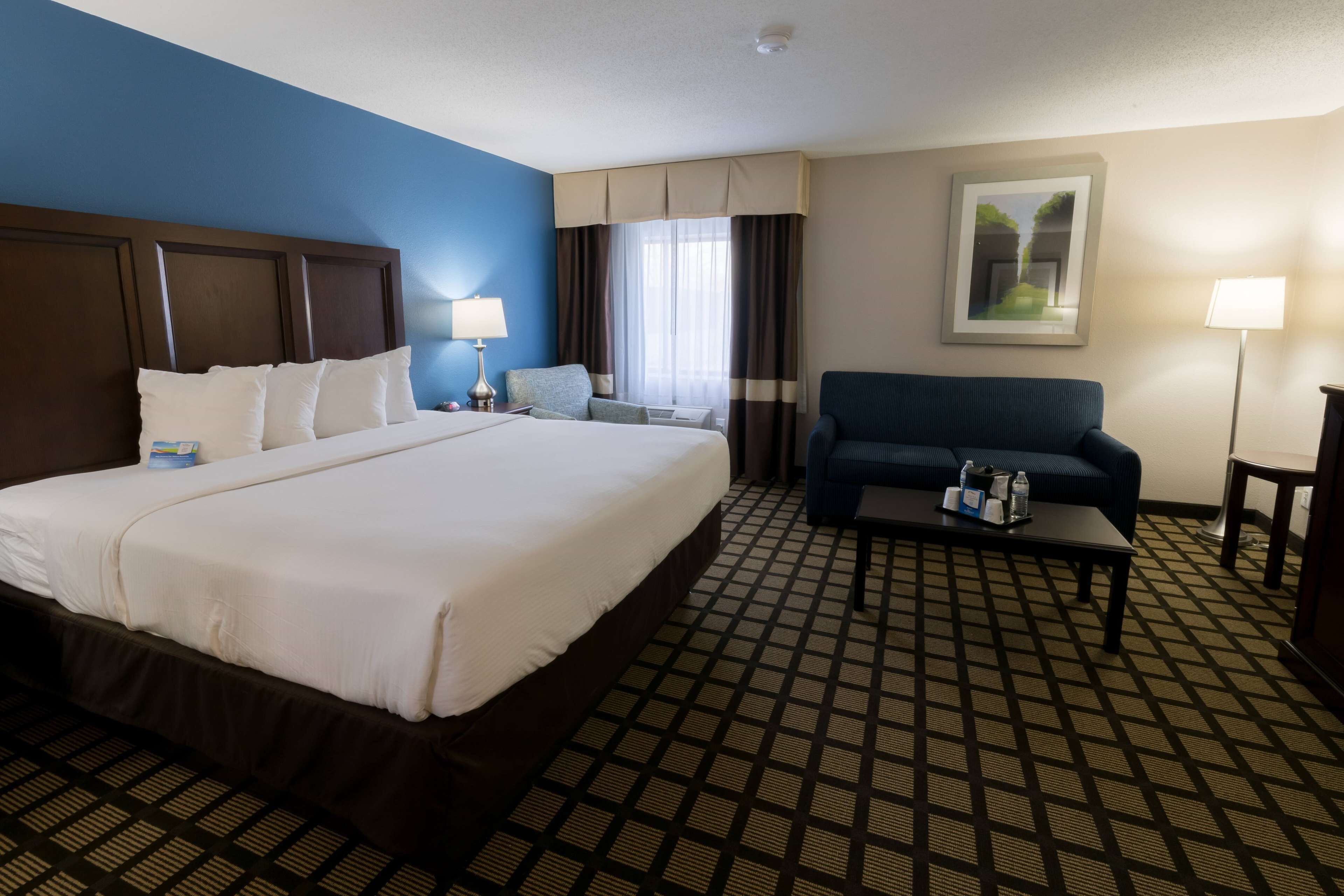 A hotel room with a large bed, a sofa, a coffee table, and a painting on the wall.