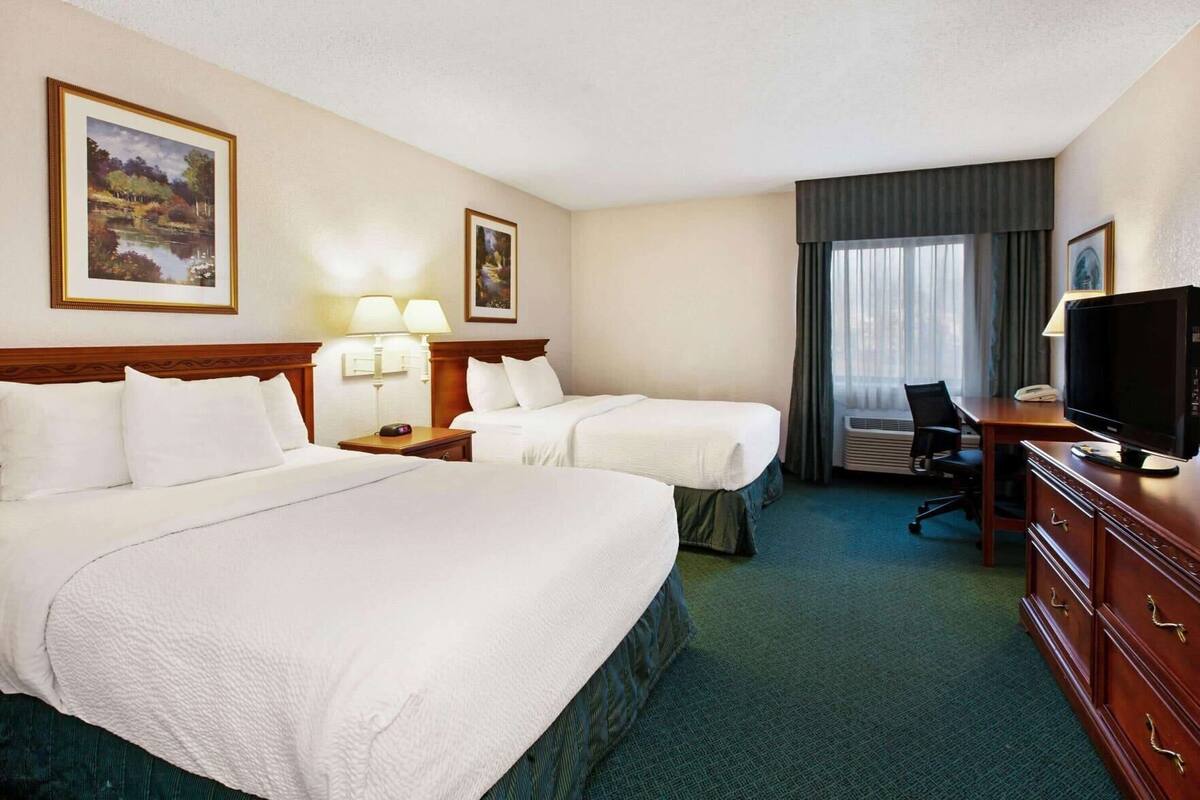 A hotel room with two beds, a desk with a television, a chair, and a window with curtains.