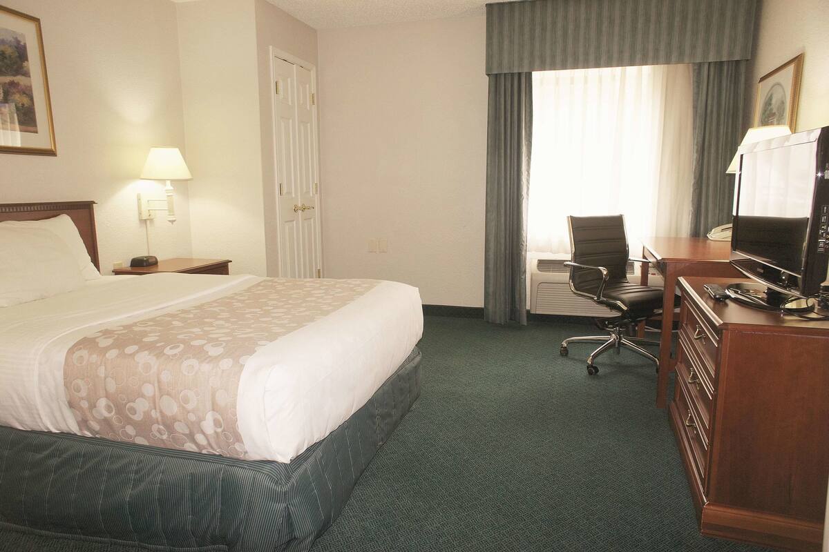 A hotel room with a large bed, a desk with a computer, a chair, and a television.