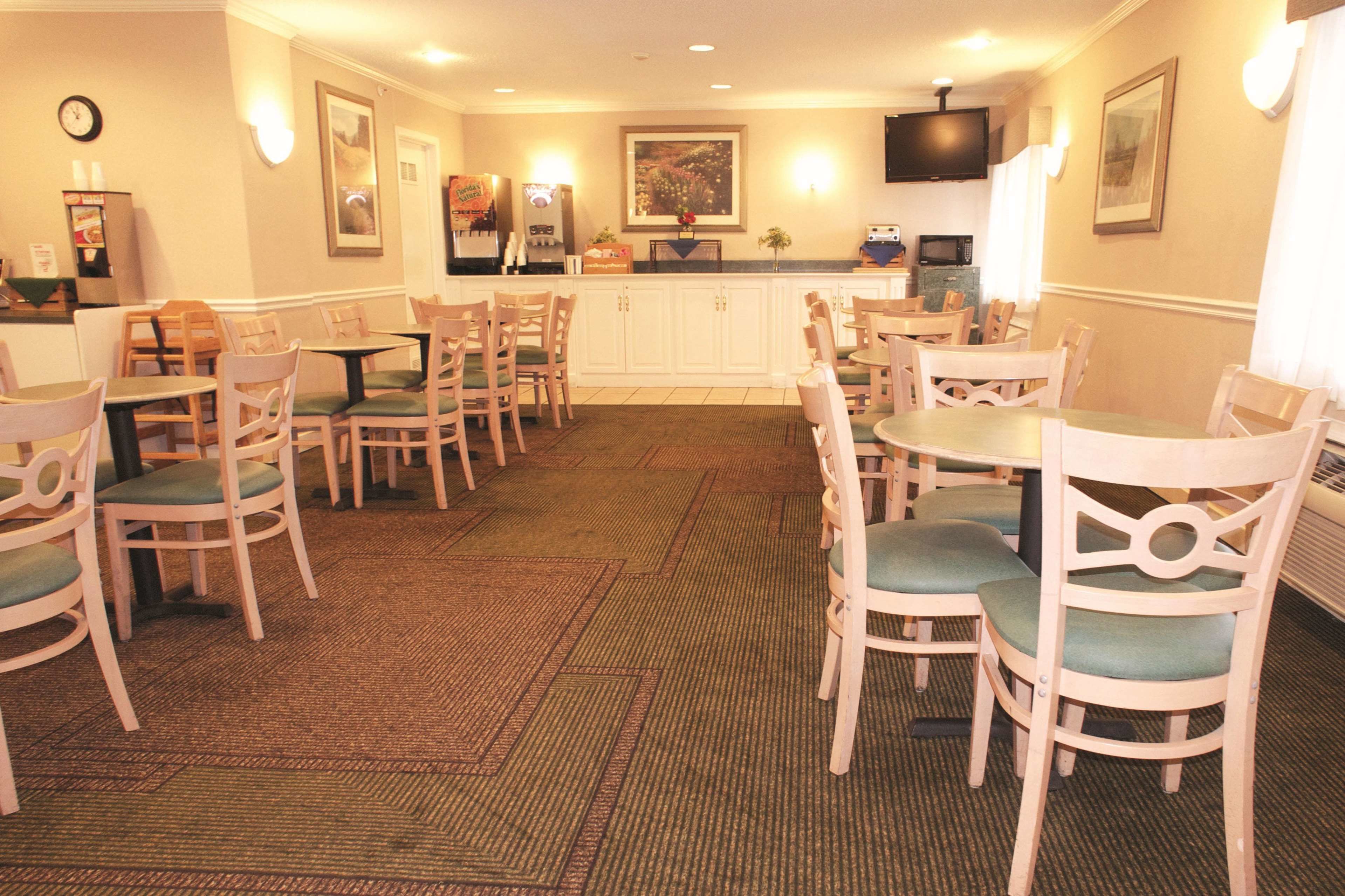 A hotel dining area with wooden tables and chairs, a clock on the wall, and a television mounted above the counter.