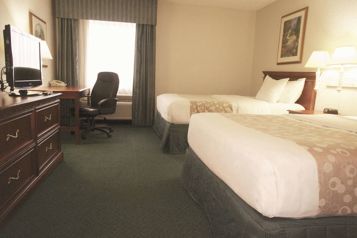 A hotel room with two beds, a desk with a computer, a chair, and a dresser.