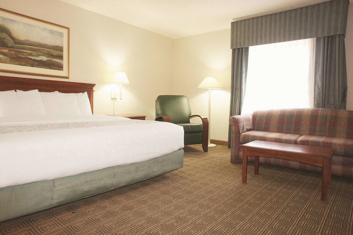 A hotel room with a large bed, a green armchair, a wooden coffee table, and a sofa.