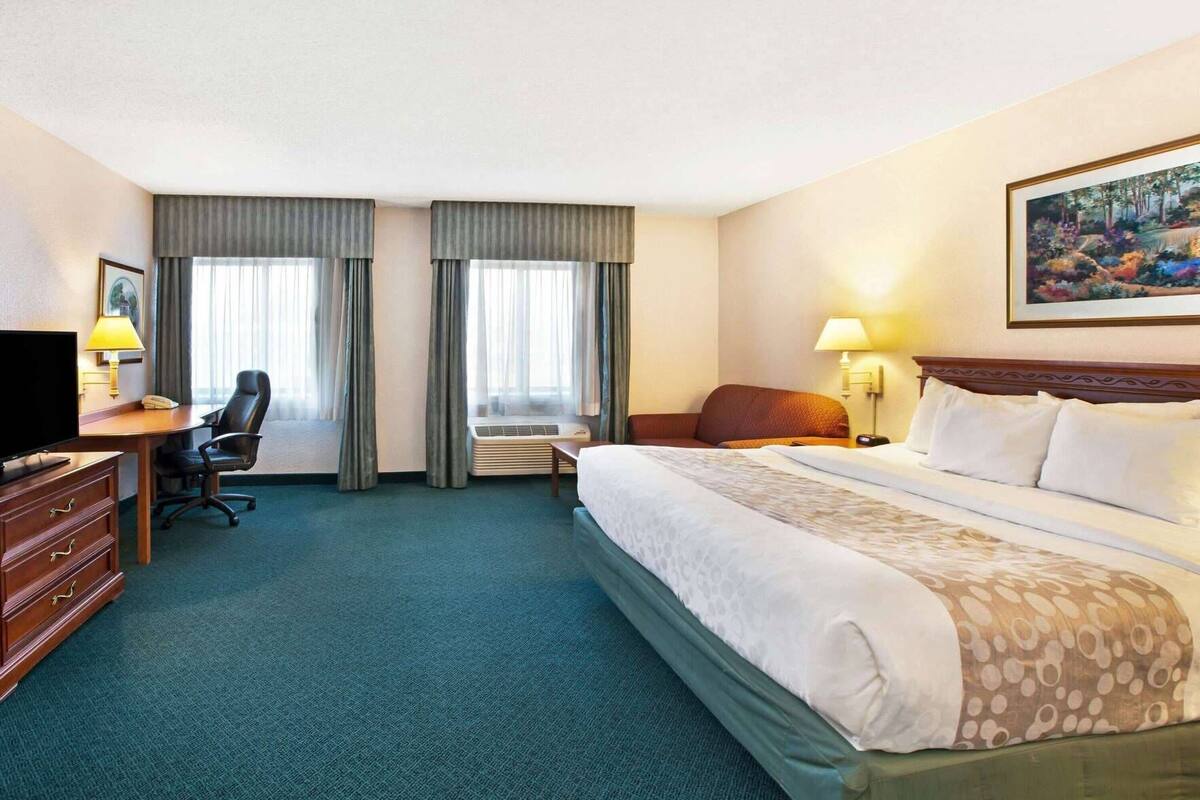 A hotel room with a bed, desk, chair, TV, and a painting on the wall.