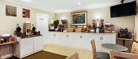 A hotel kitchen with white cabinets, a coffee station, and a television mounted on the wall.