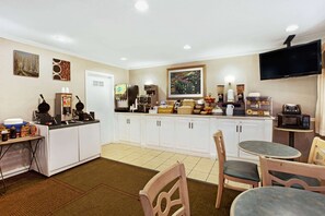 A hotel kitchen with white cabinets, a coffee station, and a television mounted on the wall.