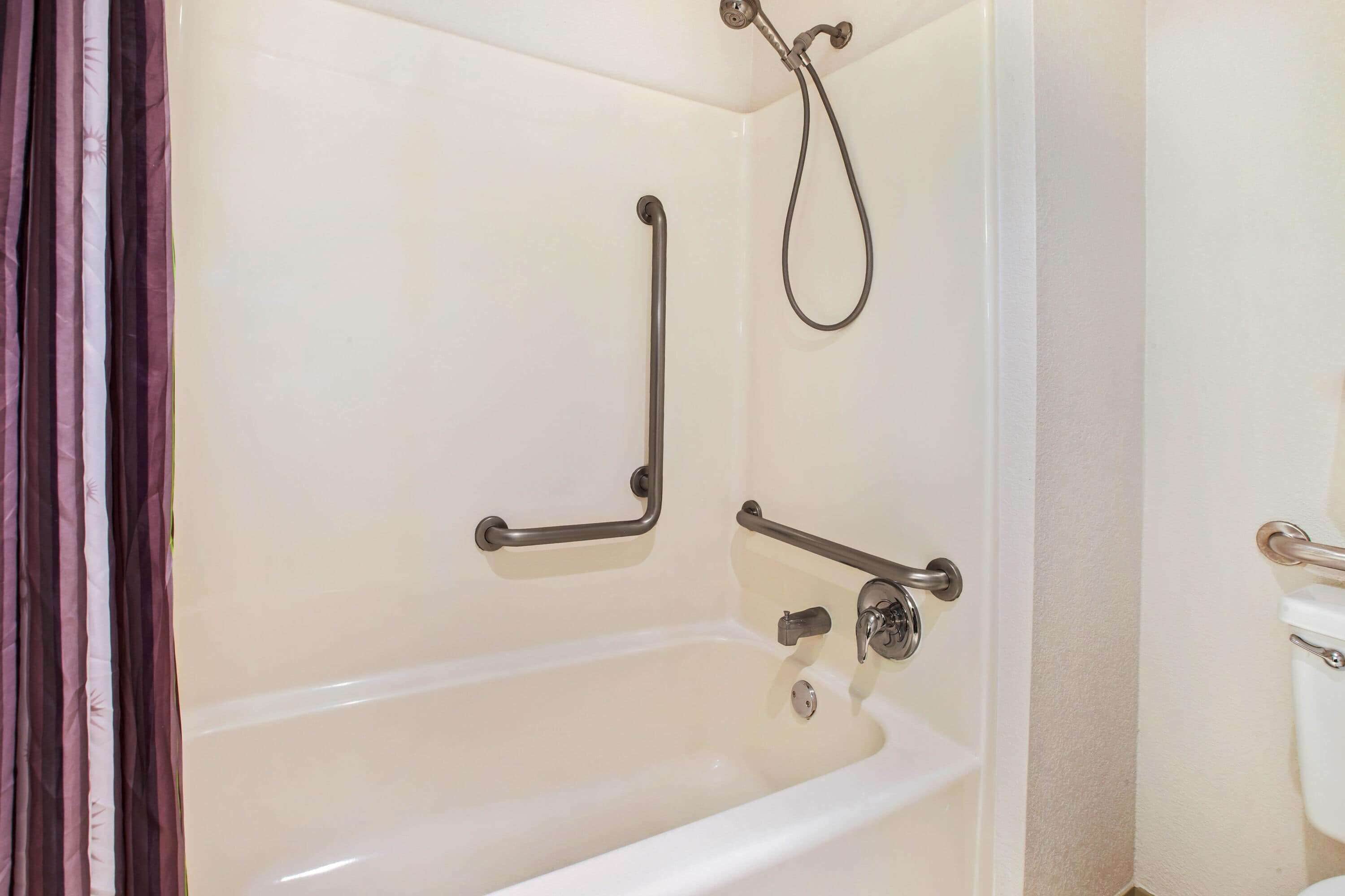 Ein Badezimmer mit Badewanne, Haltegriffen, Duschkopf und Toilette.