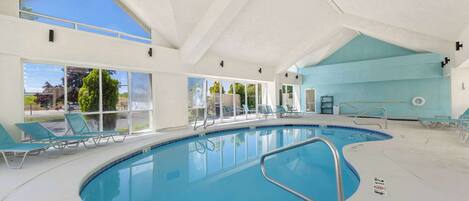 An indoor swimming pool with clear glass walls, a high ceiling, and a view of the outside.