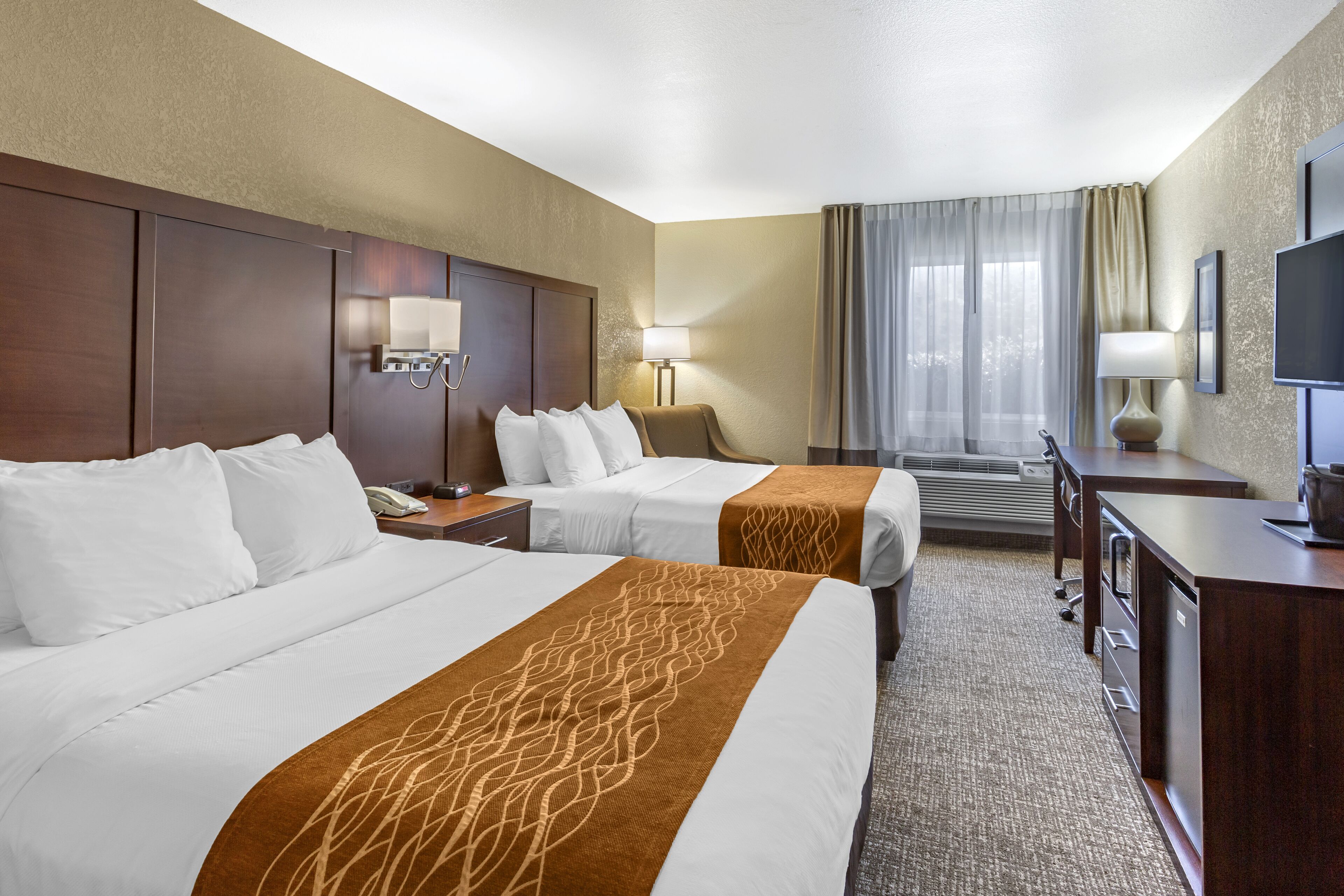 A hotel room with two beds, a desk, a chair, a TV, and a window with curtains.