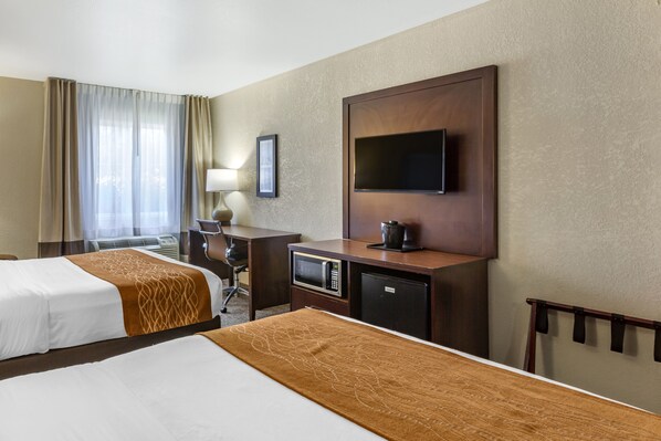 A hotel room with two beds, a desk, a television, and a microwave.