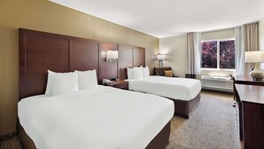 Een hotelkamer met twee bedden, een bureau, een stoel, een lamp en een raam met gordijnen.