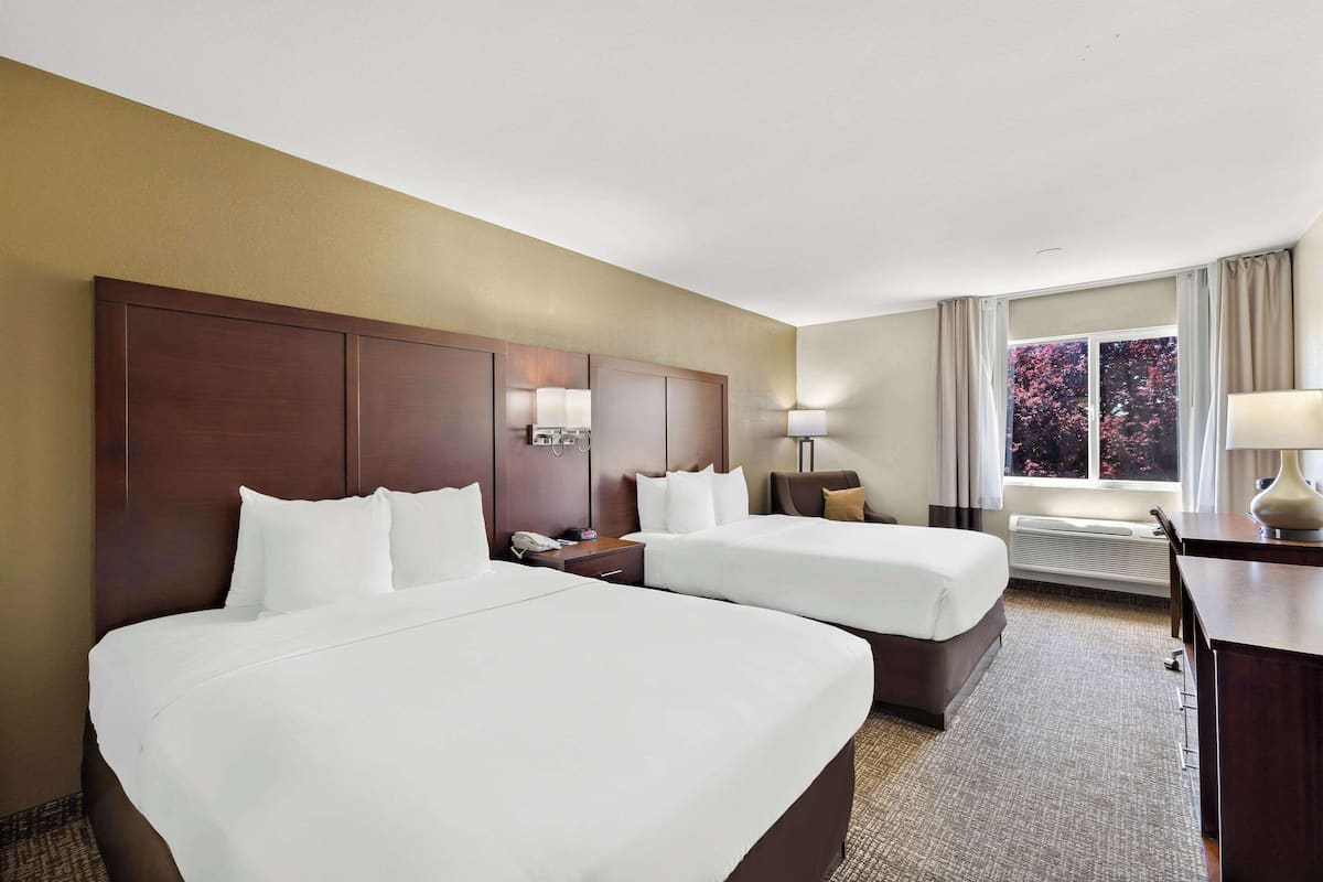 Une chambre d’hôtel avec deux lits, un bureau, une chaise, une lampe et une fenêtre avec des rideaux.