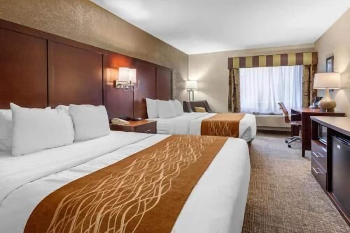 Une chambre d’hôtel avec deux lits, un bureau, une chaise et une lampe.