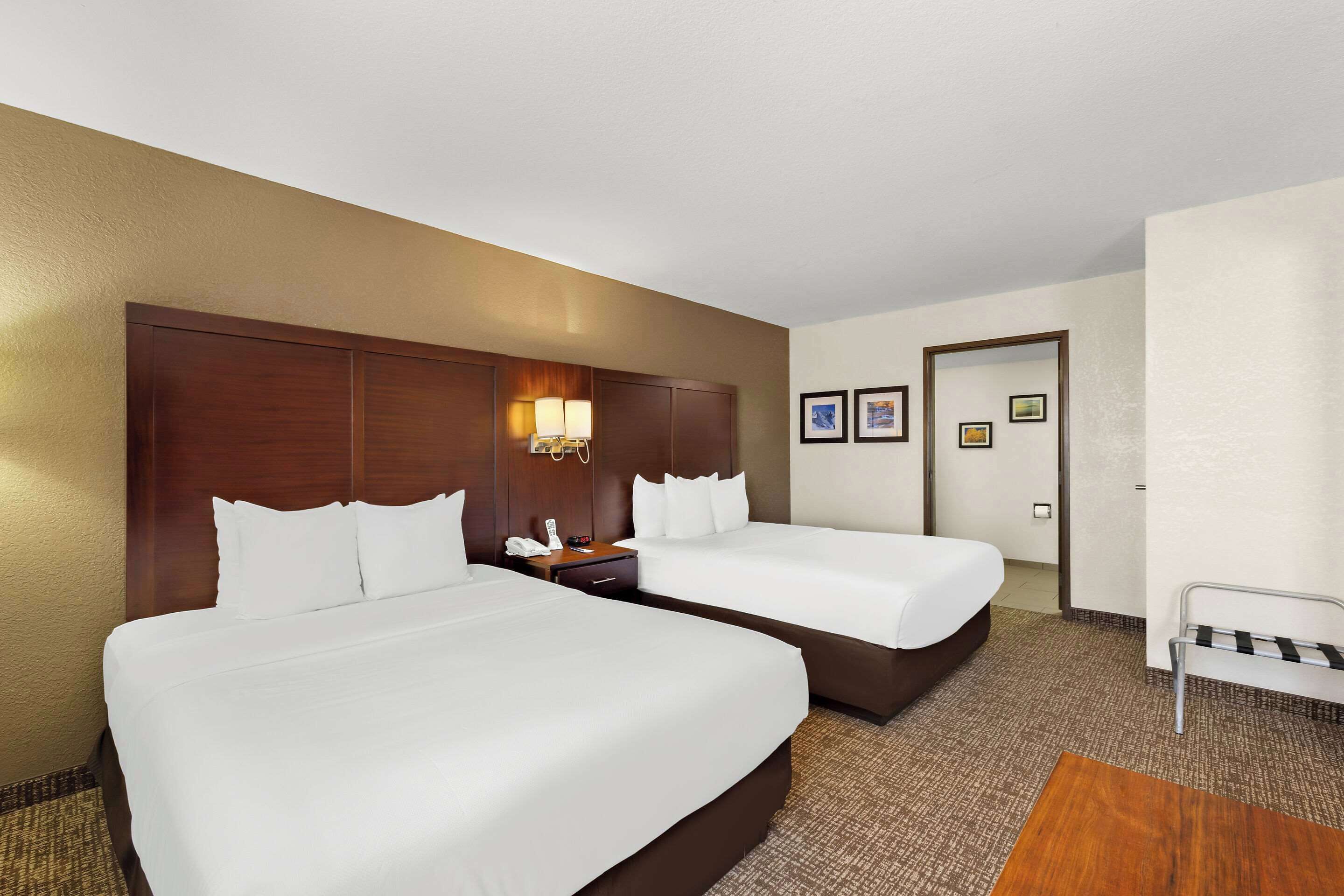 A hotel room with two beds, a wooden headboard, a nightstand with a lamp, and a small seating area.
