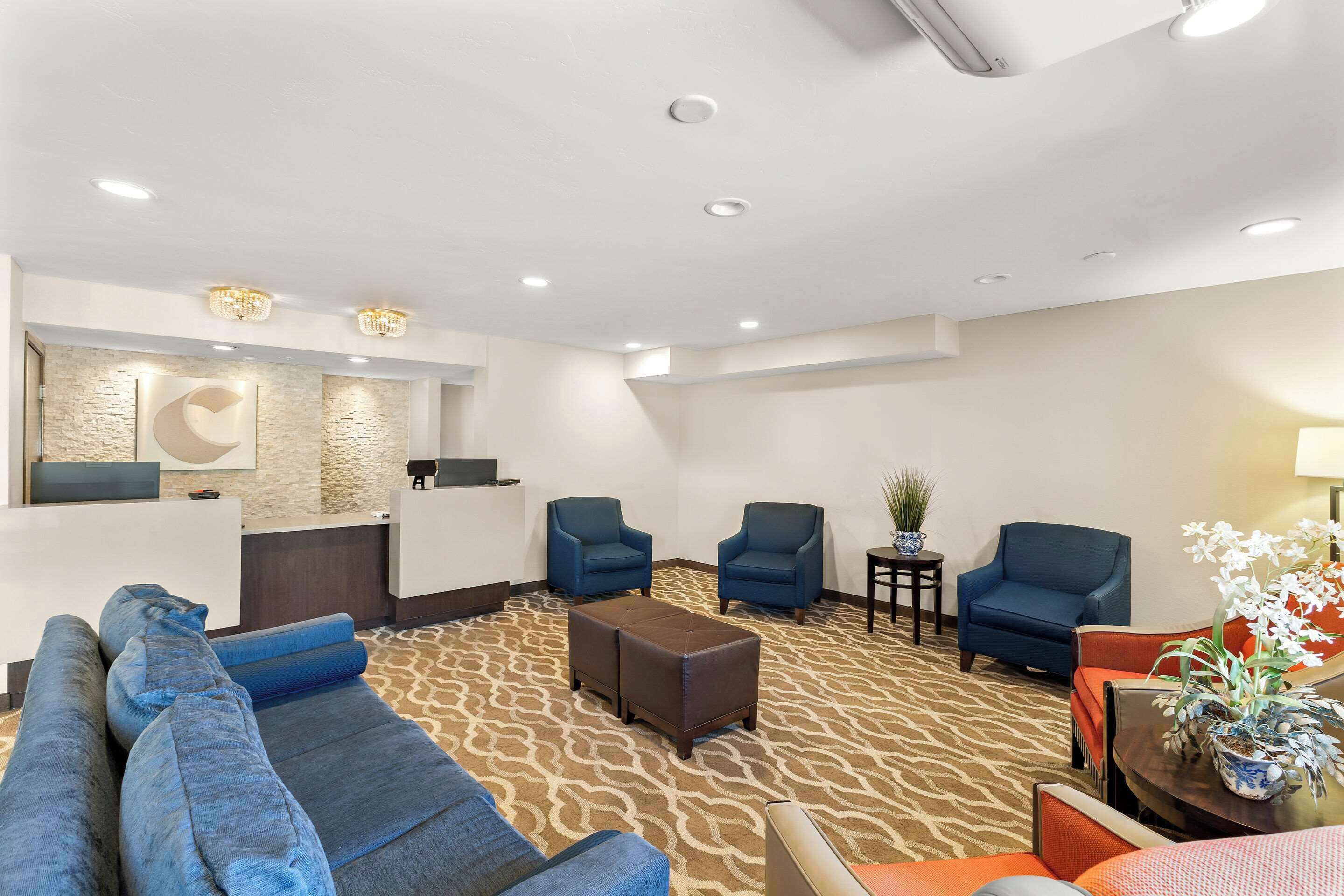 Un hall d’hôtel avec un comptoir d’accueil, des fauteuils bleus, un canapé et une moquette à motifs.