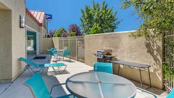 Un área de patio al aire libre con una mesa redonda y sillas azules, una parrilla y vistas a un edificio con un letrero.