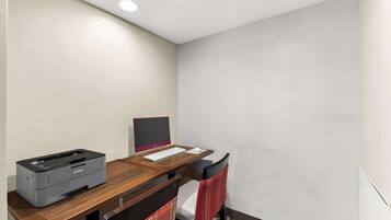 A hotel room with a wooden desk, a Brother printer, a computer monitor, and a red chair.