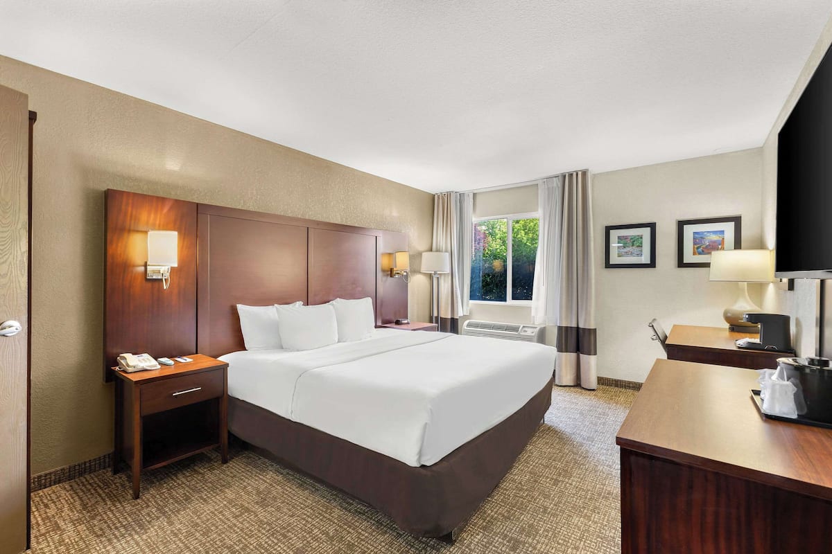 Une chambre d’hôtel avec un grand lit, une table de chevet avec une lampe, un bureau avec une lampe et une fenêtre avec des rideaux.