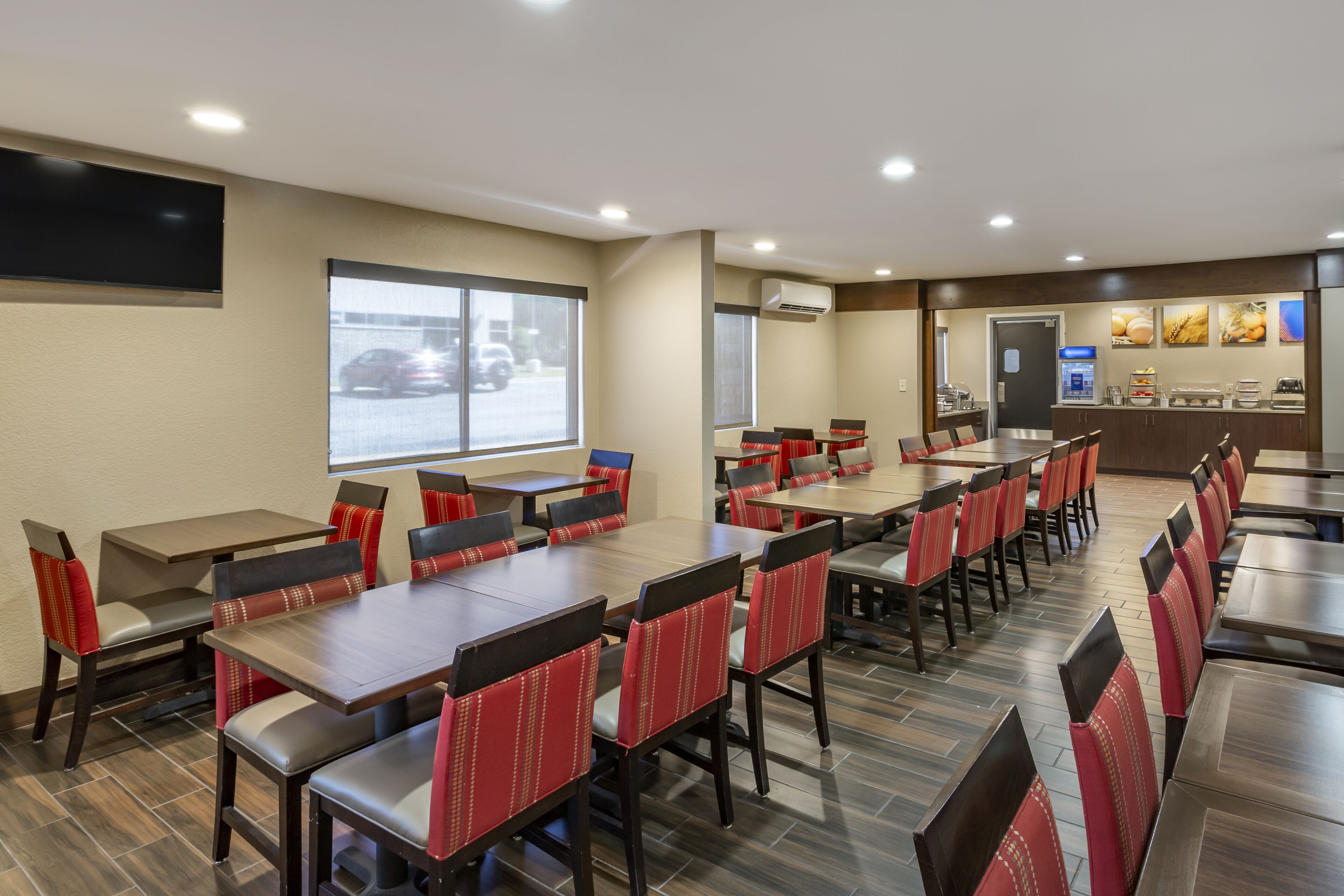 A hotel dining area with multiple tables and chairs, a large window, and a food display counter.