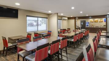 A hotel dining area with multiple tables and chairs, a large window, and a food display counter.