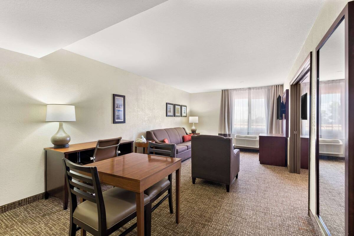 Une chambre d’hôtel équipée d’une table à manger, de chaises, d’un canapé et d’une grande fenêtre avec des rideaux.
