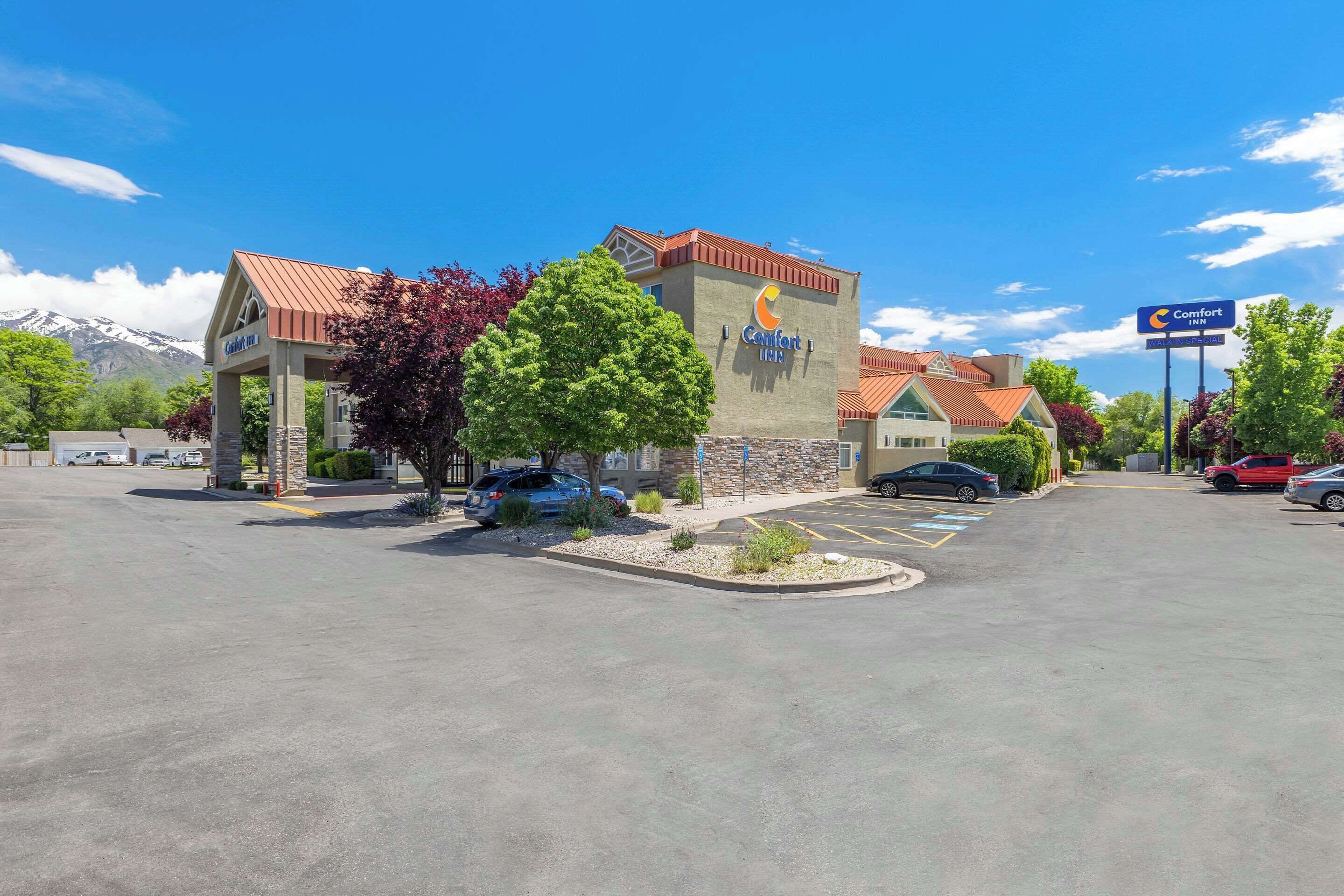 A Comfort Inn hotel with a mountain backdrop, a parking lot, and a clear sky.