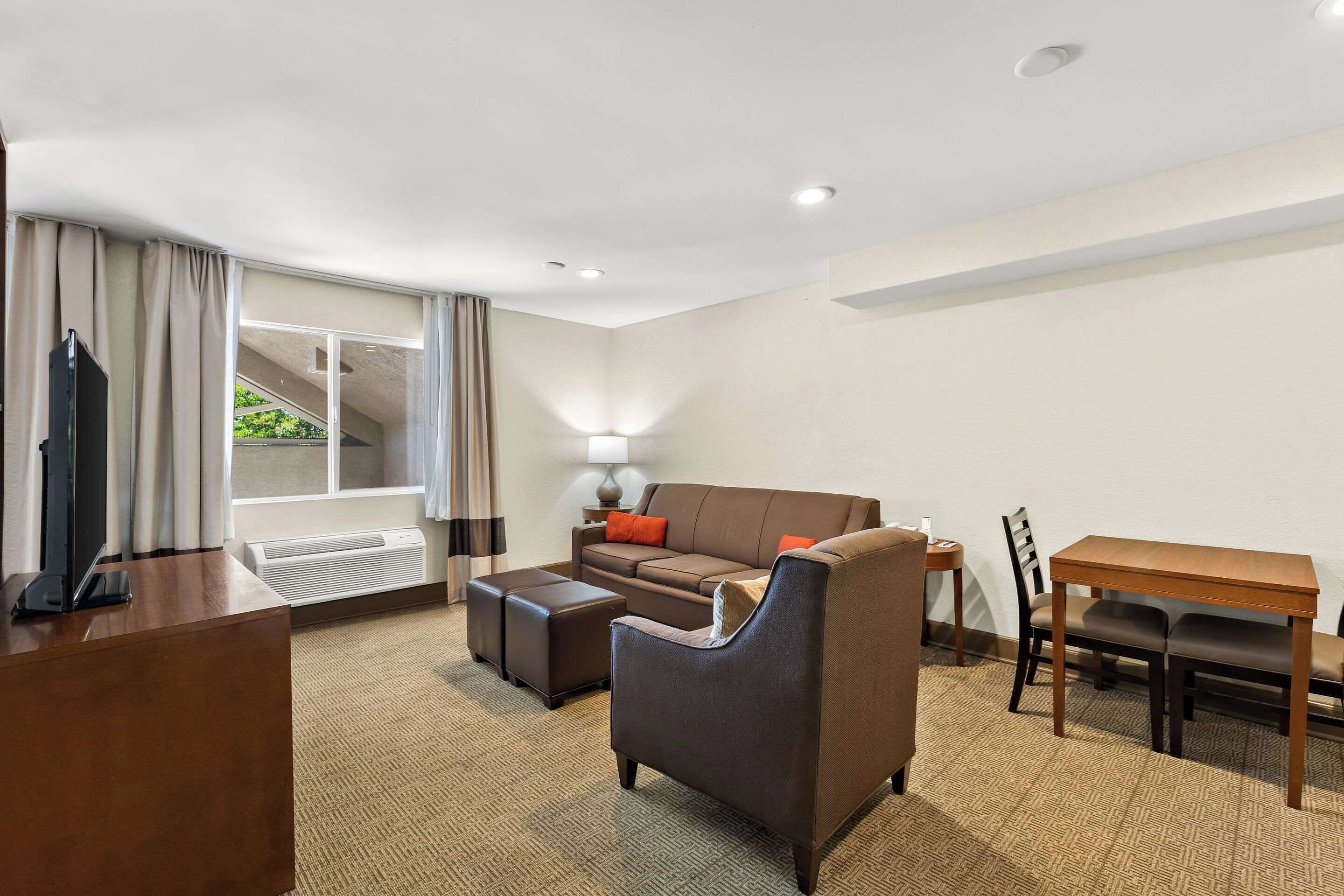 A hotel room with a sofa, armchair, wooden table, and a TV.